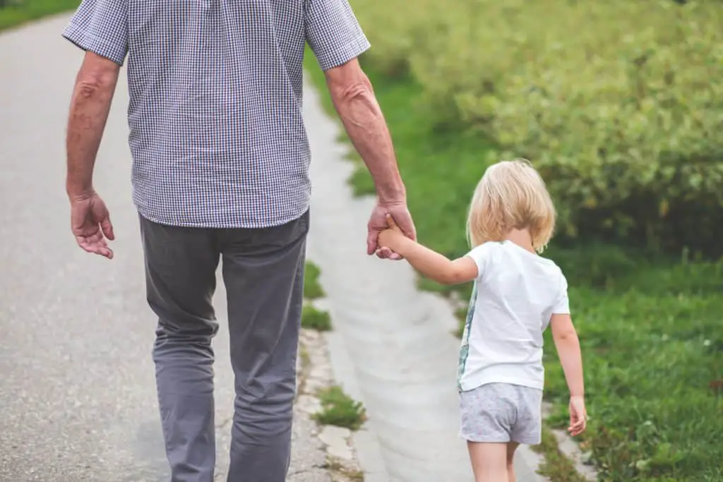 older man holding granddaughter walking down path